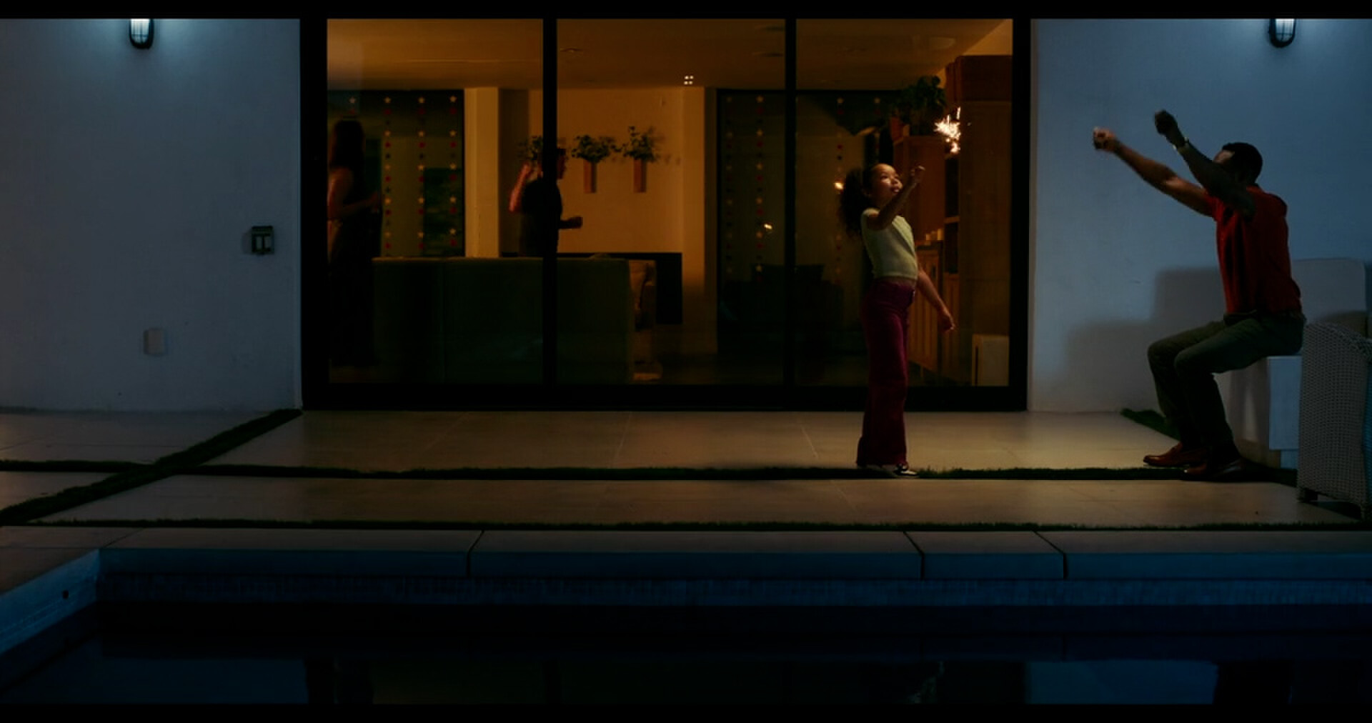 Willy and his daughter Grace play with sparklers beside a pool at night.